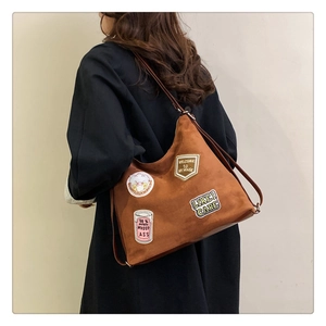 Detail of brown suede tote bag featuring unique embroidered patches on a model