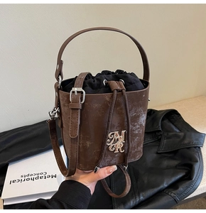 Détail du sac seau vintage en cuir marron avec logo métallique et cordon de serrage