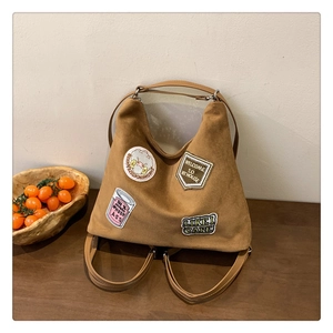 Detail view of large dark camel tote bag featuring vintage patches and suede texture