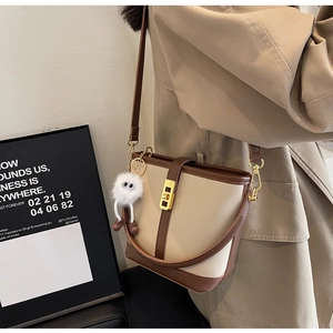 Detail of cream and brown crossbody bucket bag with gold clasp and plush charm