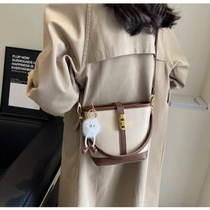 Detail of crossbody bucket bag in beige and brown leather with fuzzy charm on a model