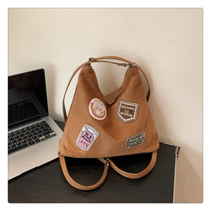 Detail of brown suede tote bag with vintage embroidery patches on a desk