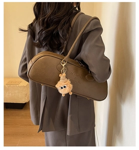 Detail view of large brown leather shoulder bag with plush charm and embossed logo