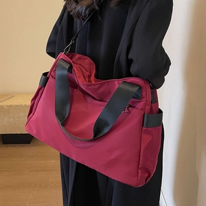 Grand sac de voyage Oxford bordeaux avec sangles noires porté par un mannequin en manteau