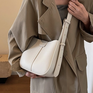 Sac seau en cuir grainé blanc avec bandoulière réglable porté sur un trench-coat
