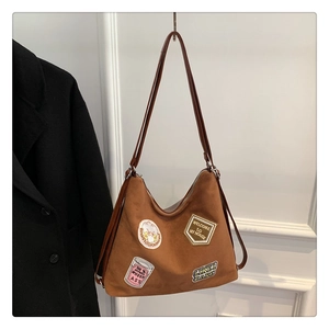 Close-up of brown suede shoulder bag with vintage embroidery patches and long strap