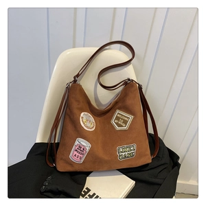 Detail of vintage brown suede tote bag with embroidered patches on a white chair