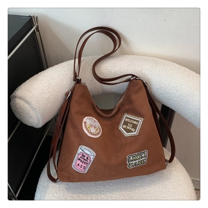 Detail of brown suede Hobo bag with artistic patches on a white textured chair