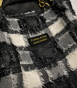 Dettaglio della borsa tote in tela a scacchi con logo in pelle nera e catena in metallo oro