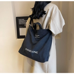 Detail view of a large black canvas tote bag worn by a model in a beige coat