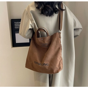 Close-up of brown canvas tote bag featuring dual straps and sleek black letter printing