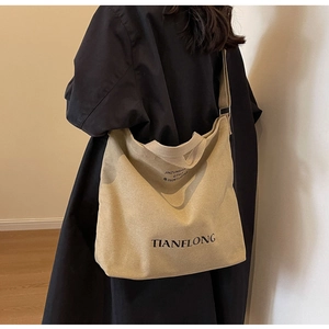 Close-up of beige canvas tote bag with black letter print on a model's shoulder