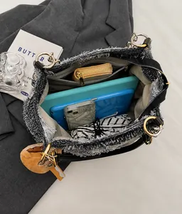 Dettaglio della borsa in denim che mostra l'interno spazioso con tablet e frange