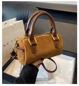 Close-up of brown suede barrel bag with gold hardware in a gift box packaging