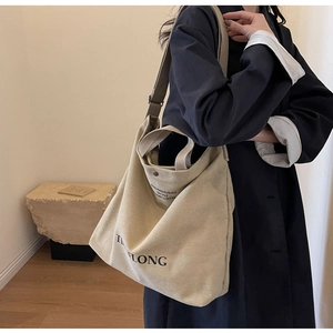 Detailed view of beige canvas tote bag featuring adjustable strap and black logo print