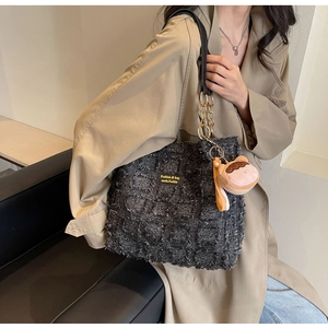 Dettaglio borsa tote in tweed con catena dorata e charm indossata con un trench