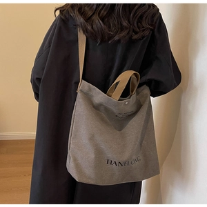 Detail of a dark grey canvas tote bag with letter print and brown shoulder straps