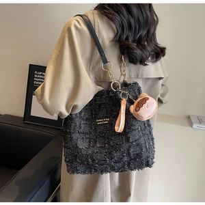 Dettaglio della borsa in tweed nero con trama sfrangiata, catena dorata e ciondolo