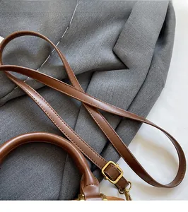 Detail of a brown leather bag showing adjustable shoulder strap and gold-tone hardware buckles