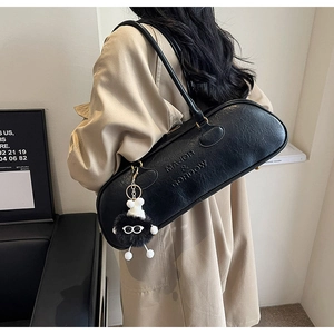 Detail of black faux leather bag with embossed logo and plush charm accessory