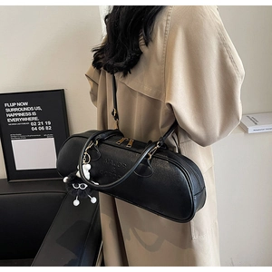 Detail of black leather Boston bag with gold hardware and plush ball charm on a model
