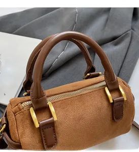Close-up of retro brown suede cylinder bag with gold hardware and zipper details