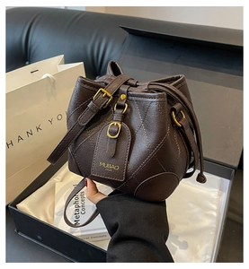 Détail d'un sac seau en cuir matelassé marron foncé avec finitions dorées et emballage cadeau