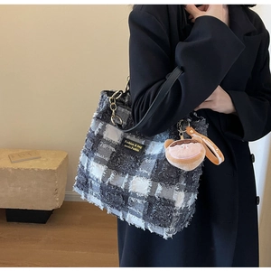 Dettaglio della borsa tote a quadri con frange, catena dorata e ciondolo peluche