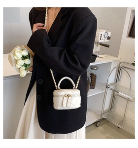 Close-up of quilted cream mini bucket bag with gold chain strap on a black blazer