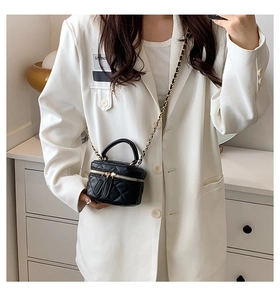 Detail of a black quilted mini square bag with gold chain strap on a white blazer