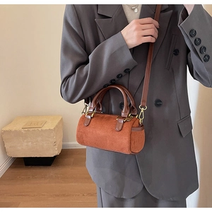 Brown frosted cylinder bag with gold hardware shown on a model in a grey suit