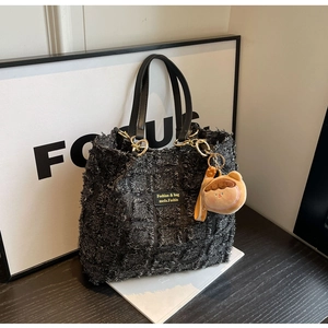 Dettaglio borsa tote in tweed a quadri neri con ciondolo orsetto e manici in pelle