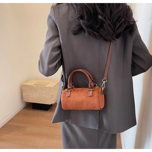 Detailed back view of a caramel suede mini Boston bag worn cross-body on a grey suit