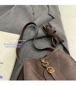 Détail du sac seau en cuir marron foncé avec coutures en losange et boucle dorée