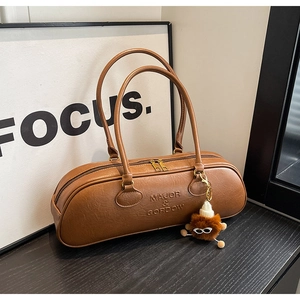 Detail of a brown leather boston bag with a plush charm and double gold zippers
