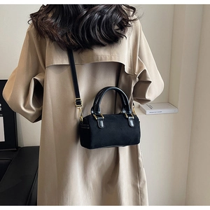 Detail of black suede Boston bag with gold hardware worn over a beige trench coat