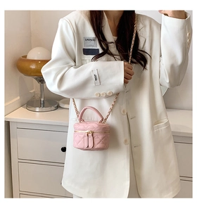 Close-up of pink quilted mini bucket bag with gold chain strap on white blazer