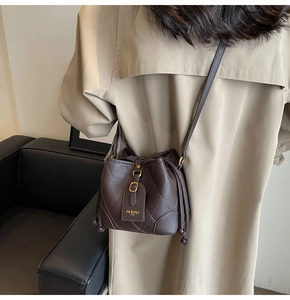 Détail d'un sac seau en cuir marron foncé avec surpiqûres matelassées et étiquette dorée