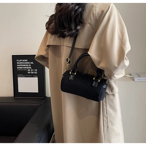 Chic black cylinder Boston bag with gold hardware worn over a khaki trench coat