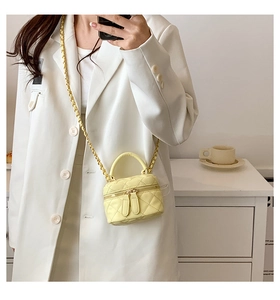 Detail of yellow quilted mini bucket bag with chain strap held by a model