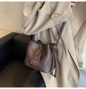 Détail d'un sac seau matelassé marron foncé avec cordon de serrage et boucle dorée