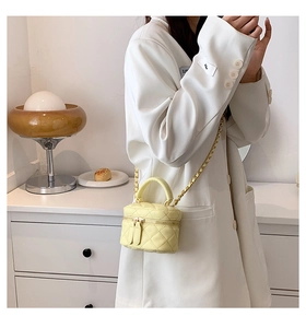 Detail of light yellow quilted mini bucket bag with gold chain strap and dual zippers