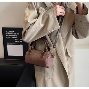 Brown frosted boston cylinder bag shown as a crossbody on a model with beige trench coat