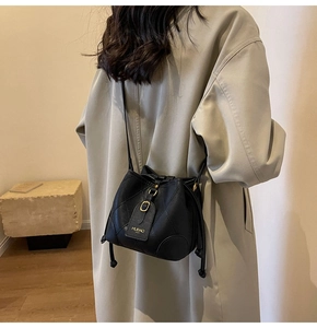 Vue détaillée du sac seau noir matelassé avec finitions dorées sur un trench-coat