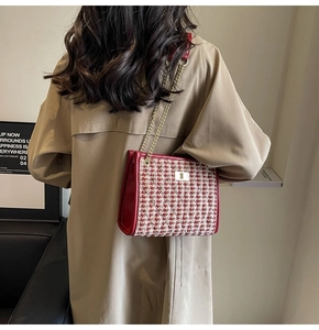 Shoulder view of a red tweed bridal bag with gold chain strap on a khaki trench coat