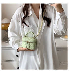 Detailed view of mint green quilted mini vanity bag with gold chain strap on white shirt