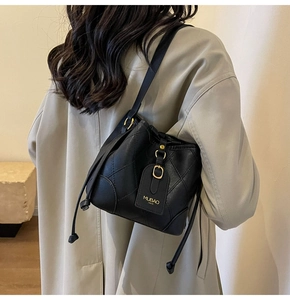 Détail d'un sac seau matelassé noir avec boucles dorées porté sur un trench beige