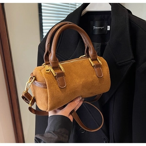 Detailed close-up of brown suede cylinder bag with leather handles and gold hardware