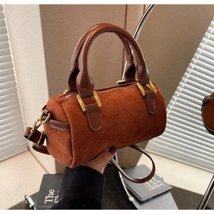 Close-up of brown suede barrel bag with leather handle and gold hardware detail