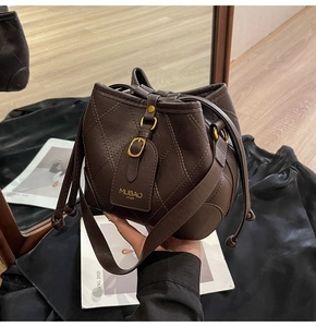 Détail d'un sac seau en cuir matelassé marron foncé avec boucle dorée et cordon de serrage